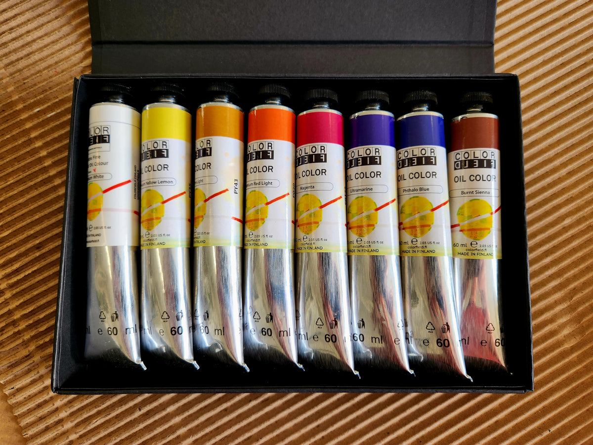 A set of eight Colorfield oil paints in a black presentation box, displayed on a brown corrugated cardboard background.